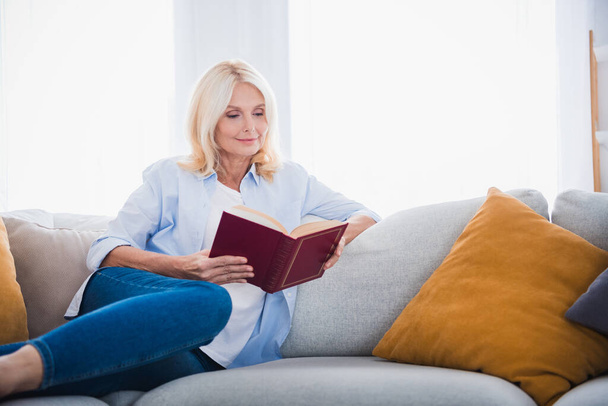 Photo portrait of attractive pensioner woman sitting sofa hold book reading enjoy morning living room modern interior decoration. - Fotó, kép