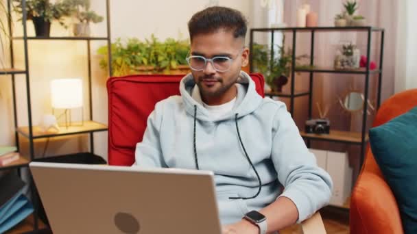 Homem indiano sentado na cadeira fechando laptop depois de terminar o trabalho na sala de estar. Jovem árabe cara freelancer trabalha on-line remoto trabalho em casa cadeira. E-learning, navegação na internet no computador notebook - Filmagem, Vídeo