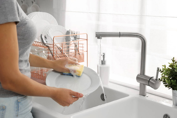 Woman washing plate at sink in kitchen, closeup - Фото, зображення
