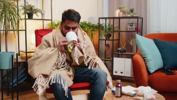Homem indiano doente em xadrez sentar sozinho tremores de frio no sofá beber chá quente em apartamento não aquecido sem aquecimento devido dívida. Unhealthy árabe cara senta-se na cadeira sentindo desconforto tentar aquecer - Filmagem, Vídeo