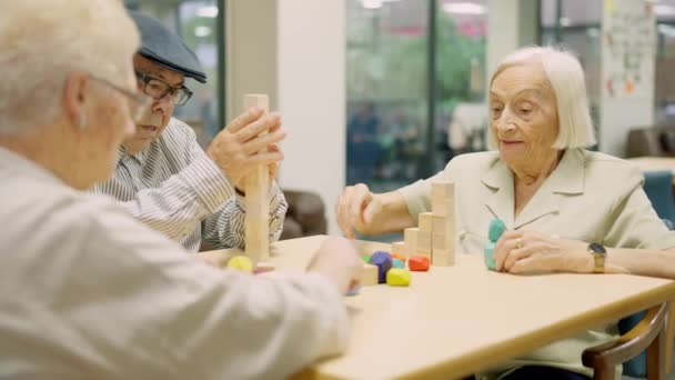 Wideo z trzech skoncentrowanych seniorów rozwiązujących gry zręcznościowe mózgu z drewnianymi kawałkami w geriatrii - Materiał filmowy, wideo