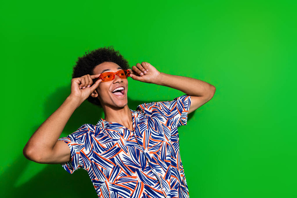 Photo of excited funky man dressed print shirt arms hands eyewear looking up empty space isolated green color background. - Фото, изображение