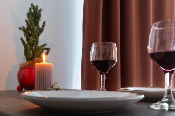 Asztalbeállítás tányérokkal, vörösborral, égő gyertyával és karácsonyfával - Fotó, kép