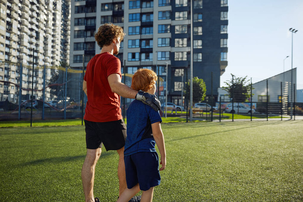 Vader en zoon kind lopen op het voetbalveld na een succesvolle wedstrijd. Familie sport recreatie activiteit concept - Foto, afbeelding