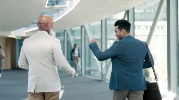Business men, fist bump and greeting to celebrate success with partner in an office building. Behind happy employees or friends walking in lobby excited about achievement, win and bonus or handshake. - Footage, Video