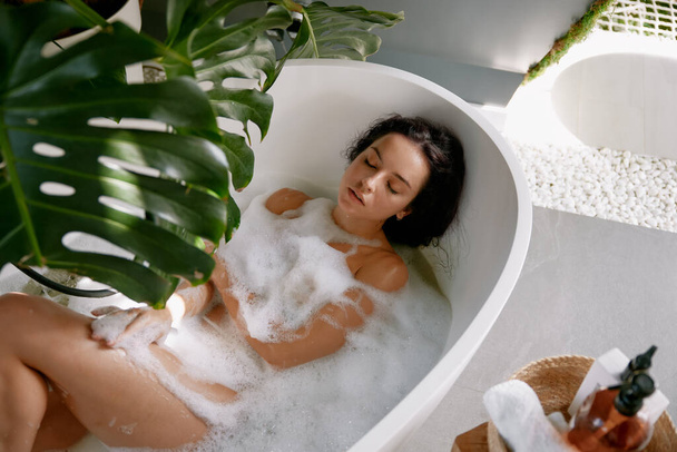 Mulher sensual relaxado desfrutando de beleza e dia spa de cuidados com a pele na banheira com espuma aromática vista de alto ângulo. Apreciação da paz e do tempo tranquilo - Foto, Imagem