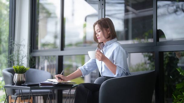 Asian businesswomen drinking coffee and checking marketing business document to taking notes in notebook while working to analyzing investment and market stock of new startup in outside office. - Photo, Image