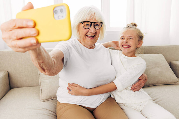 Video valkoinen isoäiti soittaa puhelimeen yhdessä hymyilevä tila ihmiset liimaus koulutus t-paita halaus perheen sisällä pojantytär lapsi valokuvaus kopioi onnea sohva kaksi selfie - Valokuva, kuva