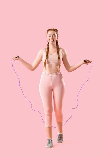 Sporty young woman jumping with rope on pink background - Photo, Image