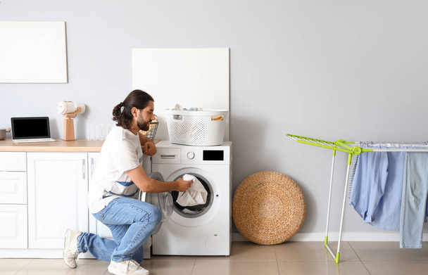 Young man putting laundry into washing machine at home - Foto, Imagen