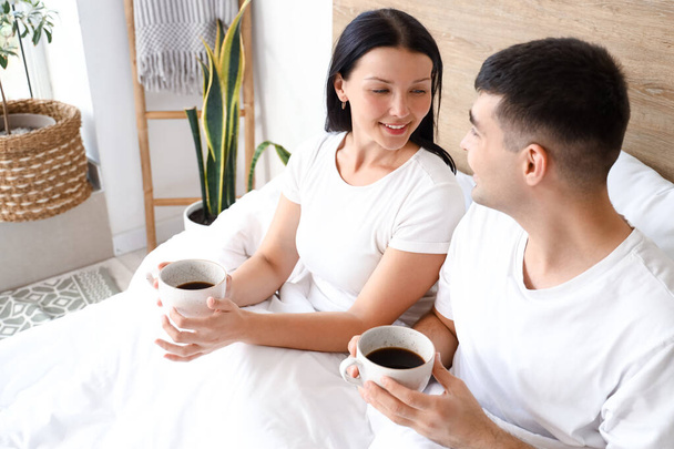 Νεαρό ζευγάρι με φλιτζάνια καφέ στην κρεβατοκάμαρα - Φωτογραφία, εικόνα