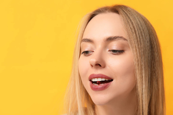 Jovem mulher tomando pílula de vitamina A no fundo amarelo, close-up - Foto, Imagem