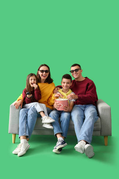 Niños pequeños con palomitas de maíz y sus padres viendo la televisión en un sofá sobre un fondo verde - Foto, Imagen
