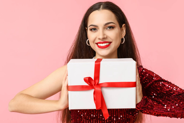 Beautiful young woman with Christmas gift on pink background - Photo, image