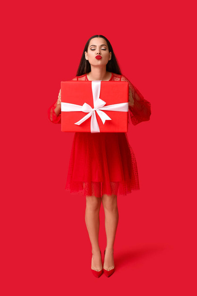 Belle jeune femme avec cadeau de Noël sur fond rouge - Photo, image