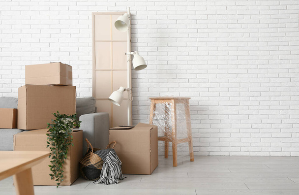 Cajas de cartón con plantas y muebles cerca de la pared de ladrillo blanco en la habitación en el día en movimiento - Foto, imagen