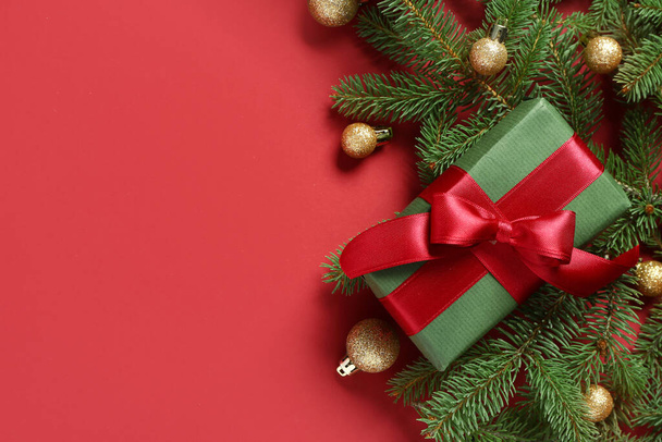 Κουτί δώρου με κλαδιά χριστουγεννιάτικου δέντρου και μπάλες σε κόκκινο φόντο - Φωτογραφία, εικόνα