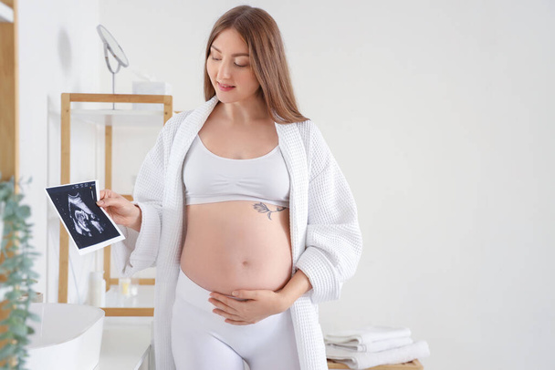 Jeune femme enceinte avec image sonogramme dans la salle de bain - Photo, image