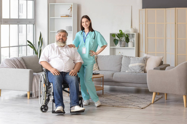 Volwassen man in rolstoel met verpleegster thuis - Foto, afbeelding