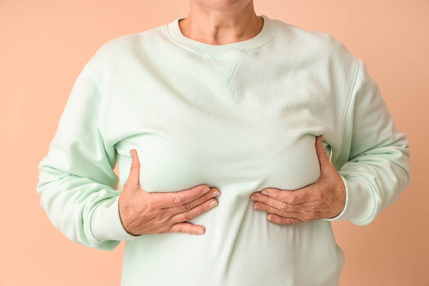 Olgun kadın göğsünü bej arka planda kontrol ediyor, yakın plan. Kanser farkındalığı kavramı - Fotoğraf, Görsel