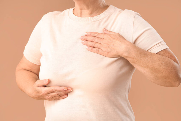 Olgun kadın göğüslerini kahverengi arka planda kontrol ediyor, yakın plan. Kanser farkındalığı kavramı - Fotoğraf, Görsel