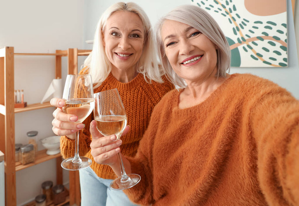 Mature female friends with glasses of wine taking selfie in kitchen, closeup - Photo, Image