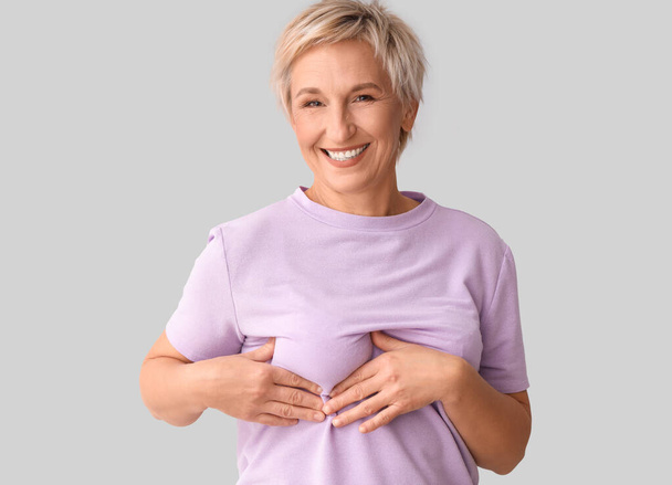 Gülümseyen olgun bir kadın, arka planda göğüslerini kontrol ediyor. Kanser farkındalığı kavramı - Fotoğraf, Görsel