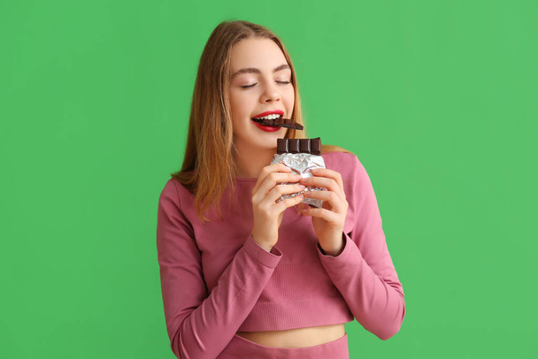 緑の背景に甘いチョコレートバーを食べる若い女性 - 写真・画像