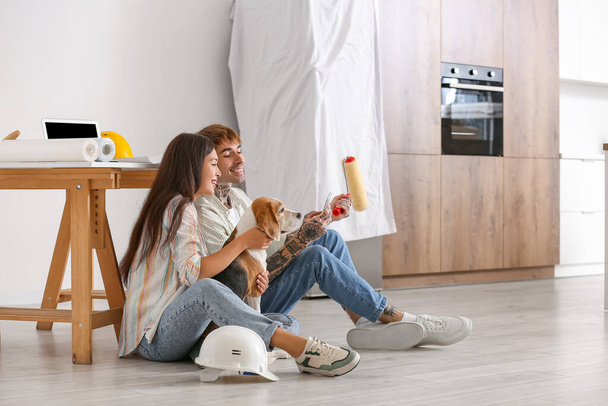 Casal jovem com cão Beagle e rolo de pintura usando telefone celular durante o reparo em sua nova casa - Foto, Imagem
