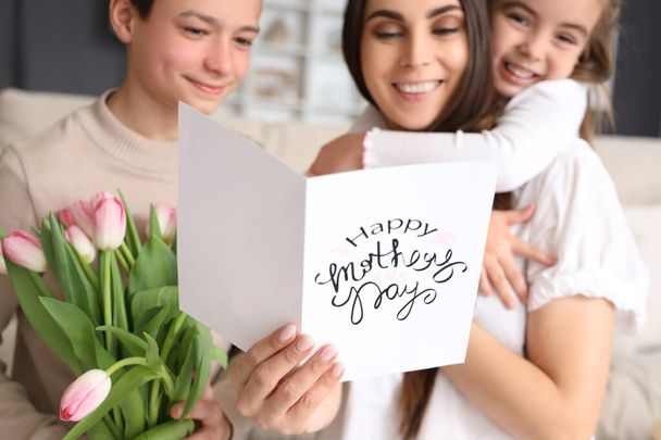 自宅にいる小さな子供たちからのメッセージカードを持った若い女性. 母の日のお祝い - 写真・画像