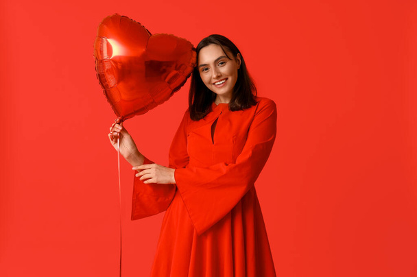 Beautiful young woman with air balloon in shape of heart on red background. Valentine's Day celebration - Photo, Image