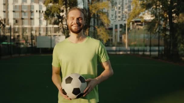 Jugador de fútbol sonriente con pelota en el campo al aire libre. Deportista sintiéndose feliz y satisfecho mirando la cámara - Metraje, vídeo