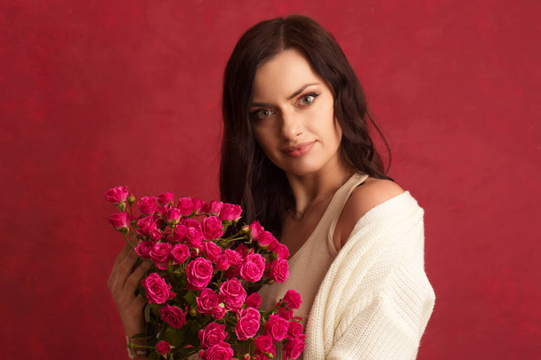 Gyönyörű fiatal barna nő egy csokor rózsaszín kis rózsa egy piros háttér - Fotó, kép