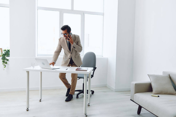 mężczyzna wideo laptop młody połączenie inteligentne biurko sukces bezprzewodowy rozmowa zwycięzca atrakcyjny profesjonalny kierownik telefonu biznesmen zadzwoń pracownik uśmiech biuro beżowy miejsce pracy biznes - Zdjęcie, obraz