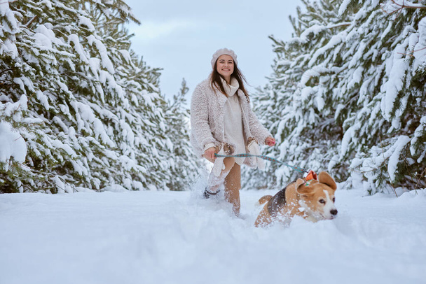девушка в зимней одежде играет с собакой Бигл зимой в снегу, зимний отдых концепции - Фото, изображение