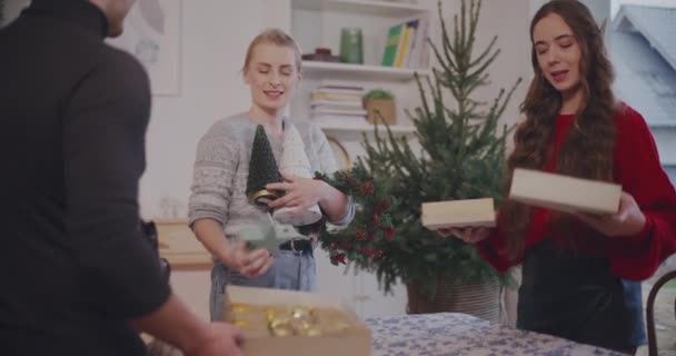Γυναίκες και άνδρες φίλοι τοποθέτηση χριστουγεννιάτικη διακόσμηση στο τραπέζι στο σπίτι κατά τη διάρκεια των διακοπών - Πλάνα, βίντεο