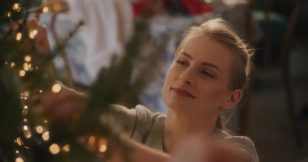Jovem mulher ajustando luzes led brilhantes na árvore em casa durante as férias de Natal - Filmagem, Vídeo