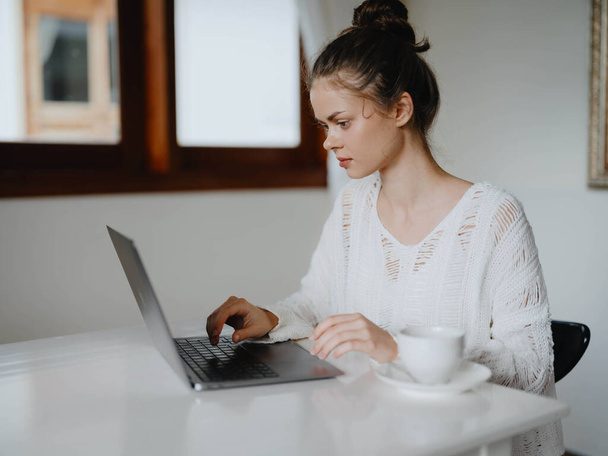 Kreatív fiatal nő dolgozik egy íróasztalnál otthon egy hangulatos belső egy csésze ital, otthoni iroda szabadúszó egy mosoly, kommunikáció és az oktatás az interneten. Kiváló minőségű fénykép - Fotó, kép