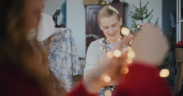 Mujeres jóvenes con luces iluminadas para la decoración de Navidad en la sala de estar durante las vacaciones - Metraje, vídeo