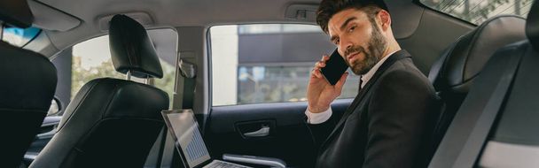 Elfoglalt vállalkozó dolgozik laptop és telefonon beszél, miközben megy a repülőtérre autóval - Fotó, kép