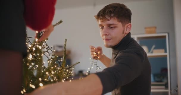 Junges Paar mit LED-Lichtern schmückt Weihnachtsbaum im Wohnzimmer - Filmmaterial, Video
