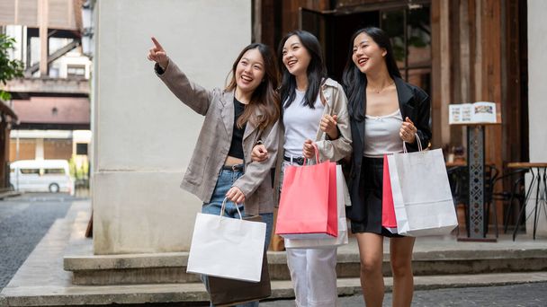 Güzel Asyalı genç kız arkadaşlar alışveriş çantalarını alıp şehirde alışveriş günlerinin tadını çıkarıyorlar. Yurt dışına seyahat, turizm, tüketim, moda ve yaşam tarzı - Fotoğraf, Görsel