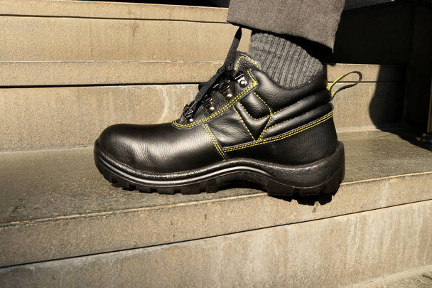 Fotografie stavebního dělníka v černé kožené bezpečnostní obuvi při práci, aby si chránil nohy - Fotografie, Obrázek