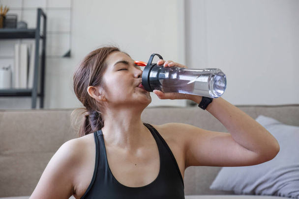 Young healthy Asian woman holds a water bottle for practicing yoga online or exercising at home.. - Photo, Image