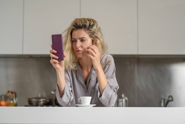 自宅のキッチンで携帯電話でチャットを疲れ不幸な女性。朝の主婦気分 - 写真・画像