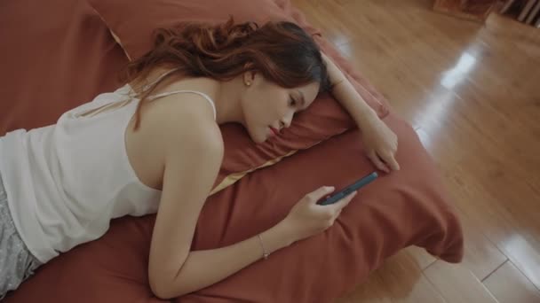 Widok z góry na dół znudzona lub zmęczona Azjatka przewijanie mediów społecznościowych podczas odpoczynku w łóżku w domu sam - Materiał filmowy, wideo