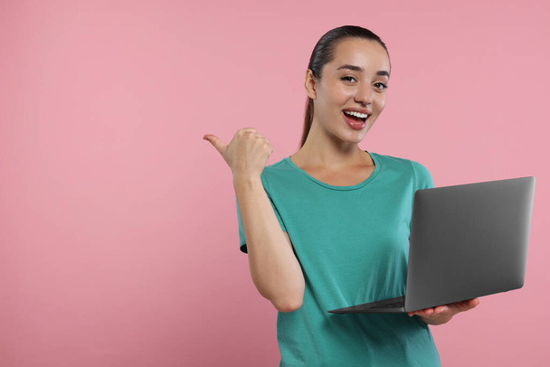 Special promotion. Smiling woman with laptop pointing at something on pink background. Space for text - Foto, Bild