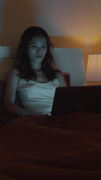 Vertical shot of female Asian workaholic using wireless computer doing report in bed at nighttime - Footage, Video