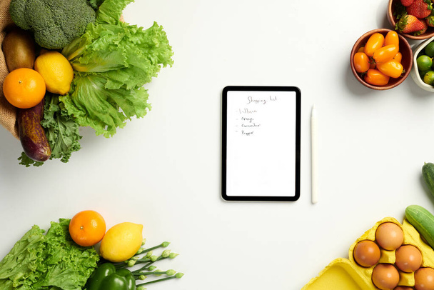 Tablet počítač s ručně psaným nákupním seznamem na stole s potravinami - Fotografie, Obrázek