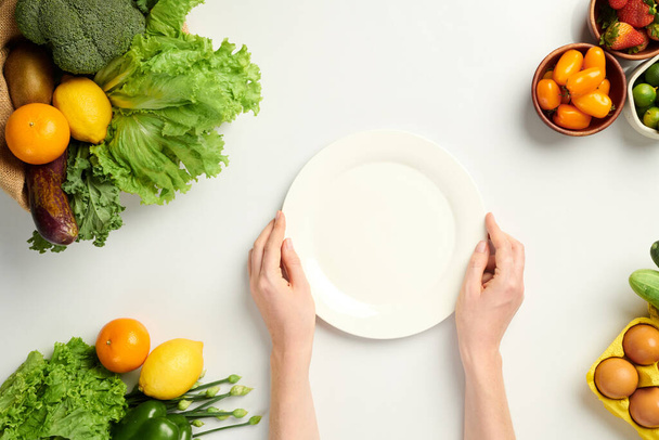Hands of person putting empty plate on table with fresh fruits and groceries, view from the top - Photo, Image